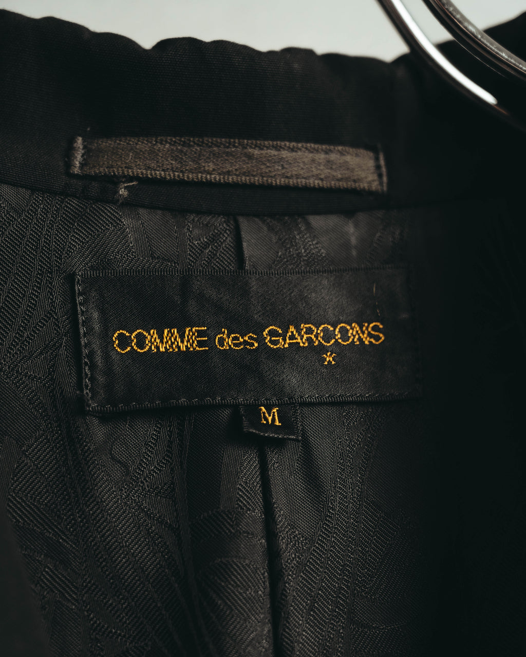 黒地に金色文字で「COMME des GARÇONS」と刺繍された旧式ブランドタグと、M表記のサイズタグを写した内側のカット。