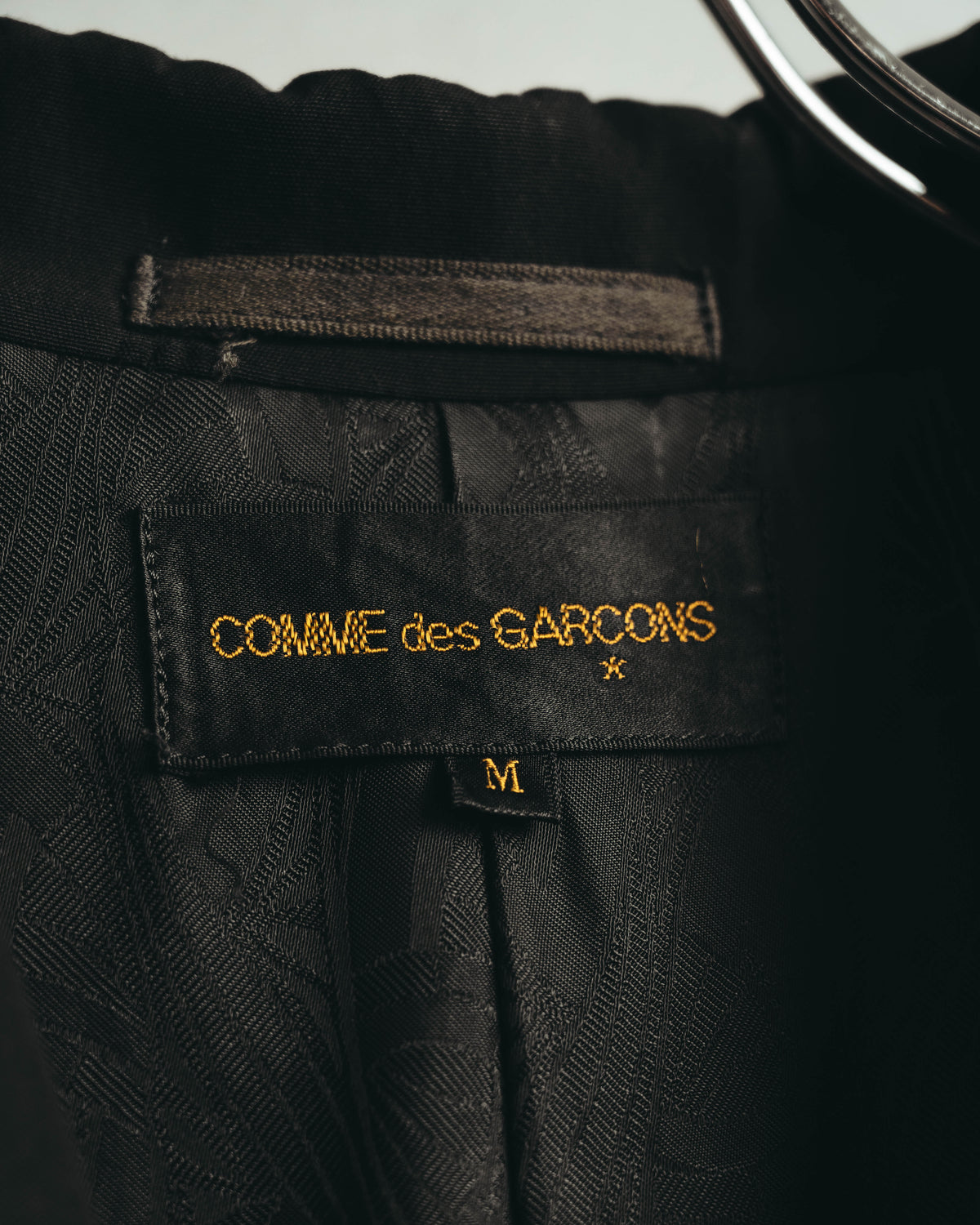 黒地に金色文字で「COMME des GARÇONS」と刺繍された旧式ブランドタグと、M表記のサイズタグを写した内側のカット。