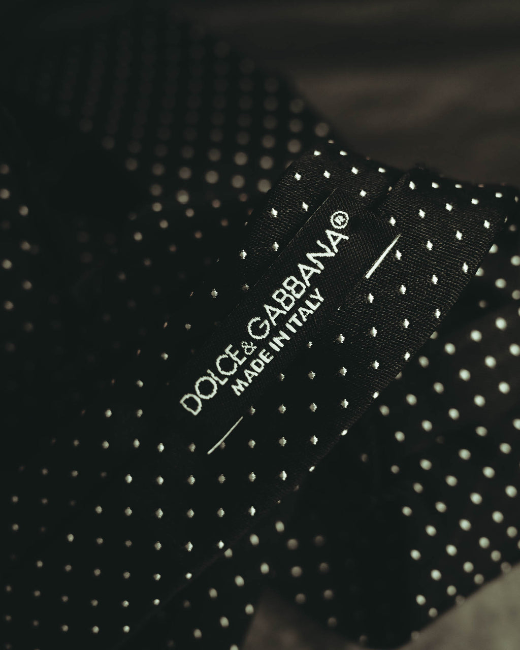 ブラック地にホワイト系の極小ドットを配したネクタイの織りタグ。Dolce & Gabbanaの表記と「MADE IN ITALY」を確認できるカット。