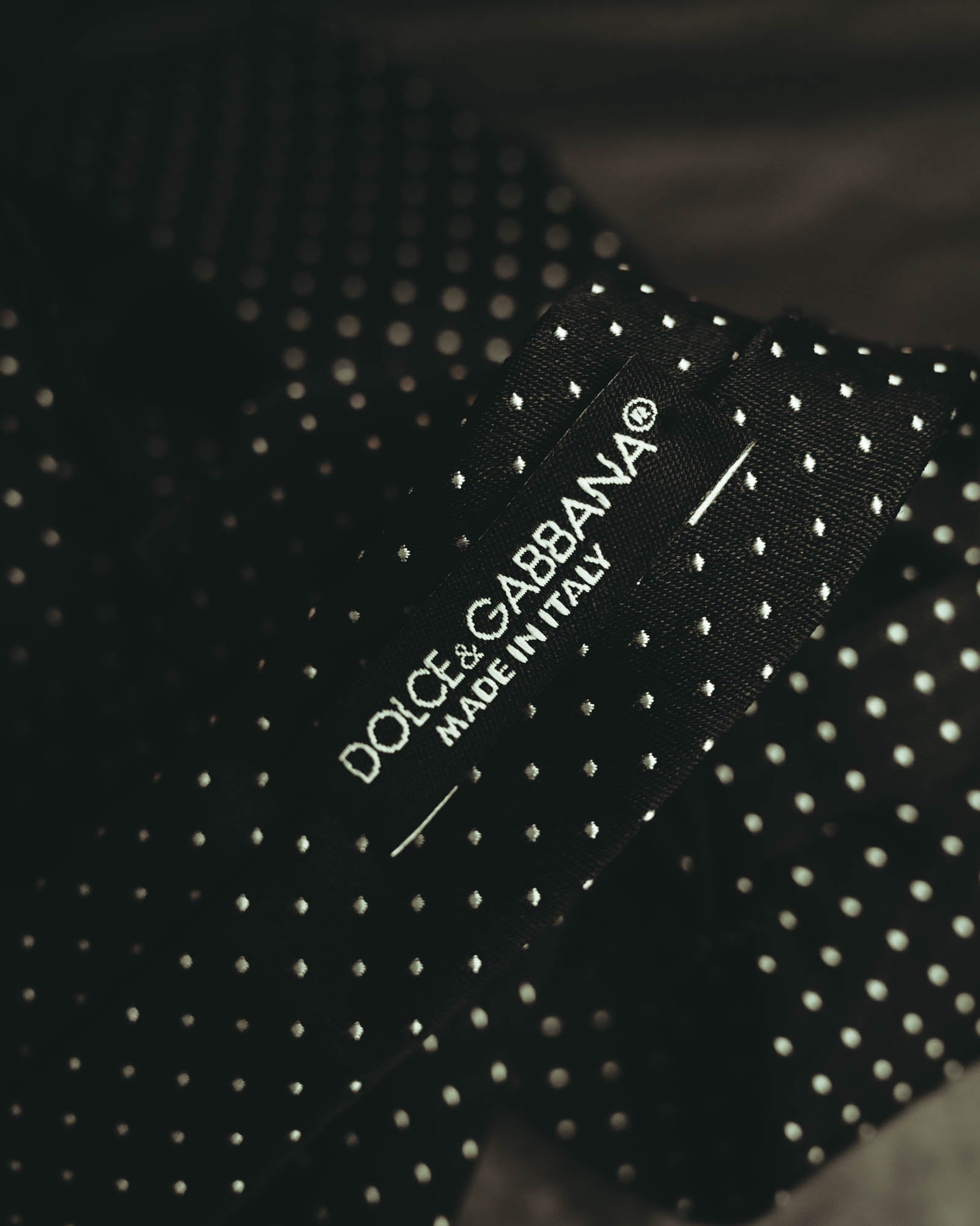 ブラック地にホワイト系の極小ドットを配したネクタイの織りタグ。Dolce & Gabbanaの表記と「MADE IN ITALY」を確認できるカット。
