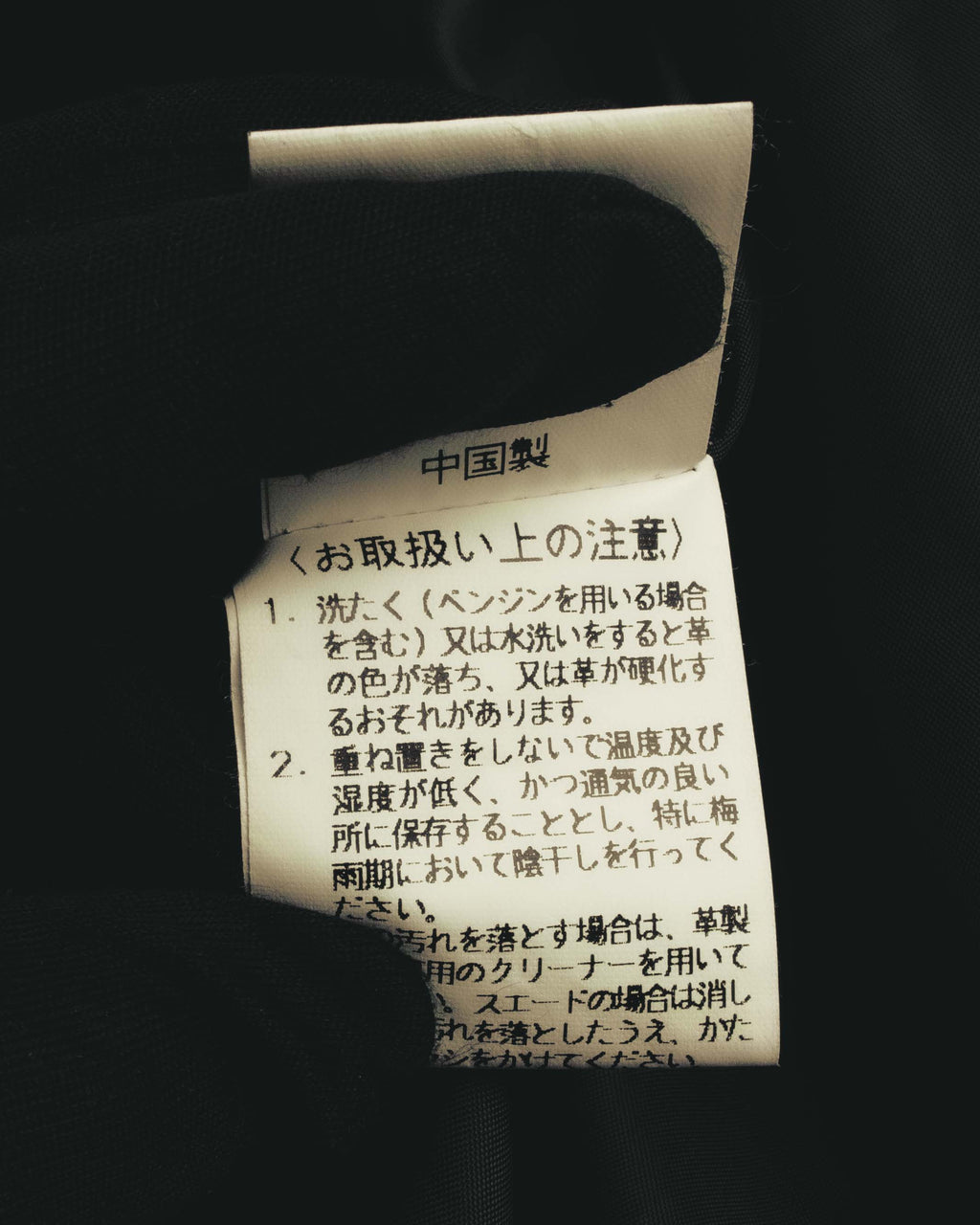 コート内側に配された取扱い表示タグのクローズアップ。中国製表記と、革製品の洗濯・保管に関する注意書きが確認できます。
