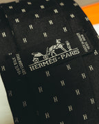 剣先に織りで表現された馬車図案と HERMES-PARIS のシグネチャーを捉えたディテールカット。ブラック地に銀白色に見えるHモチーフのジャカード織りも確認できます。