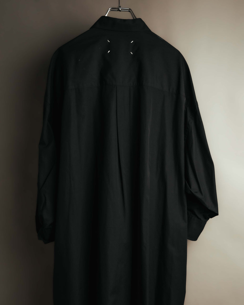 ロングシャツドレスの背面全体を捉えたカット。ネック下に配された4本の白いステッチと、裾へ流れる背面のプリーツを確認できます。