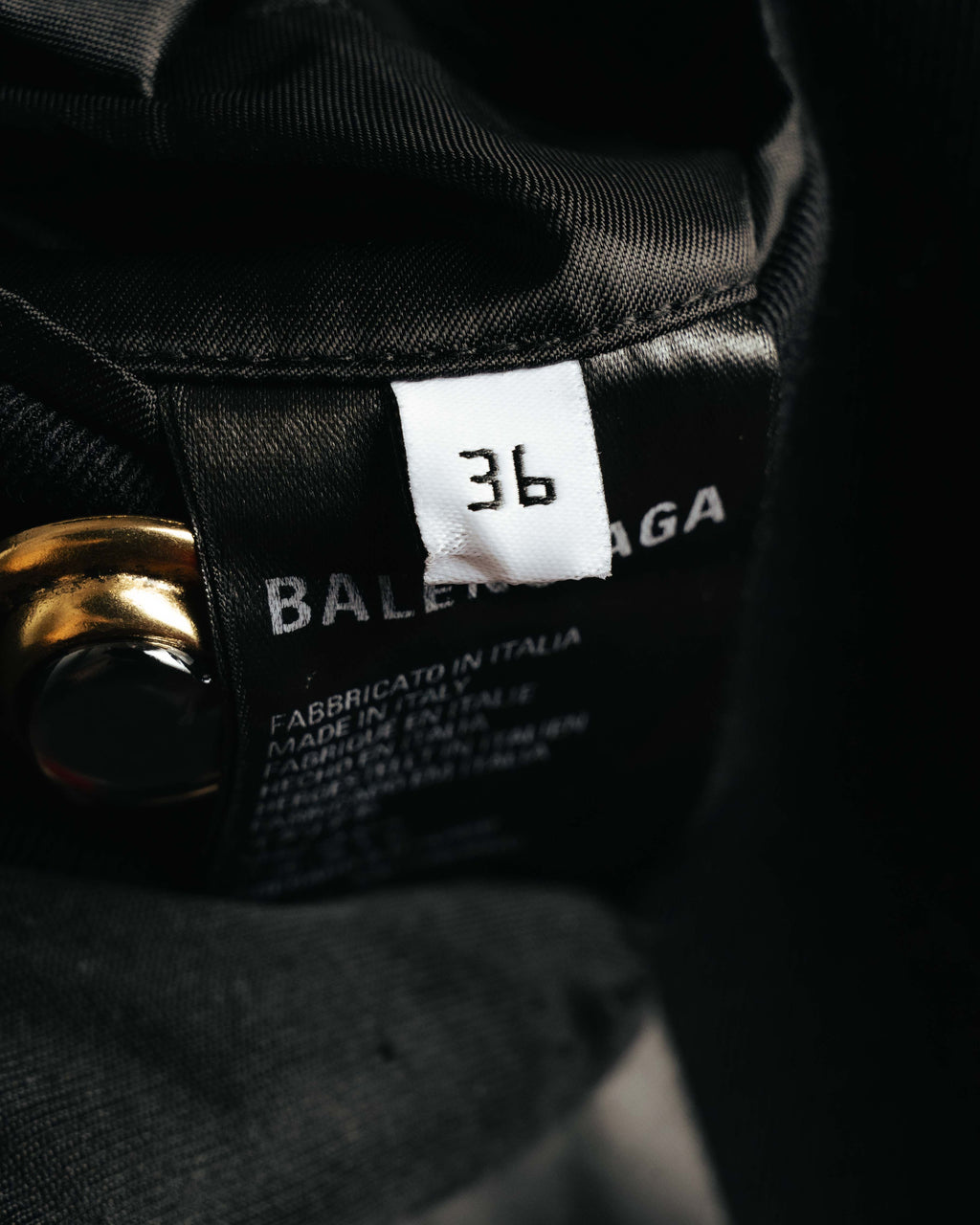 襟元内側に配されたBALENCIAGA PARIS表記のブランドタグと、36表記のサイズタグを捉えたカット。周囲にはブラックの裏地とゴールドカラーの金属パーツが見える。