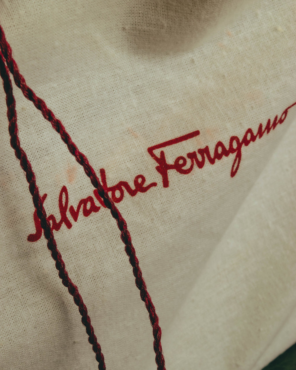 アイボリーの布製保存袋に、赤い筆記体で施されたSalvatore Ferragamoロゴのクローズアップ。