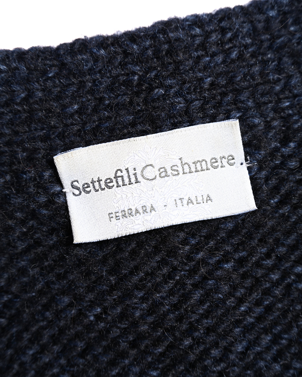 「Settefili Cashmere」と「FERRARA - ITALIA」の表記を確認できる、ダークネイビーのチャンキーニット内側のブランドネームタグ。