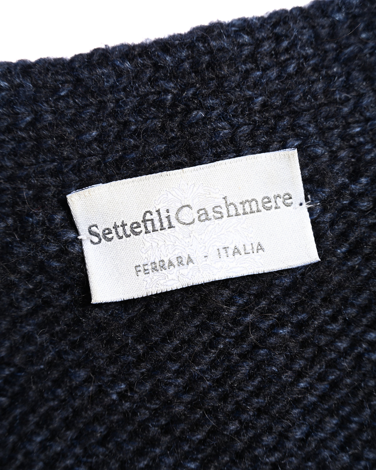 「Settefili Cashmere」と「FERRARA - ITALIA」の表記を確認できる、ダークネイビーのチャンキーニット内側のブランドネームタグ。