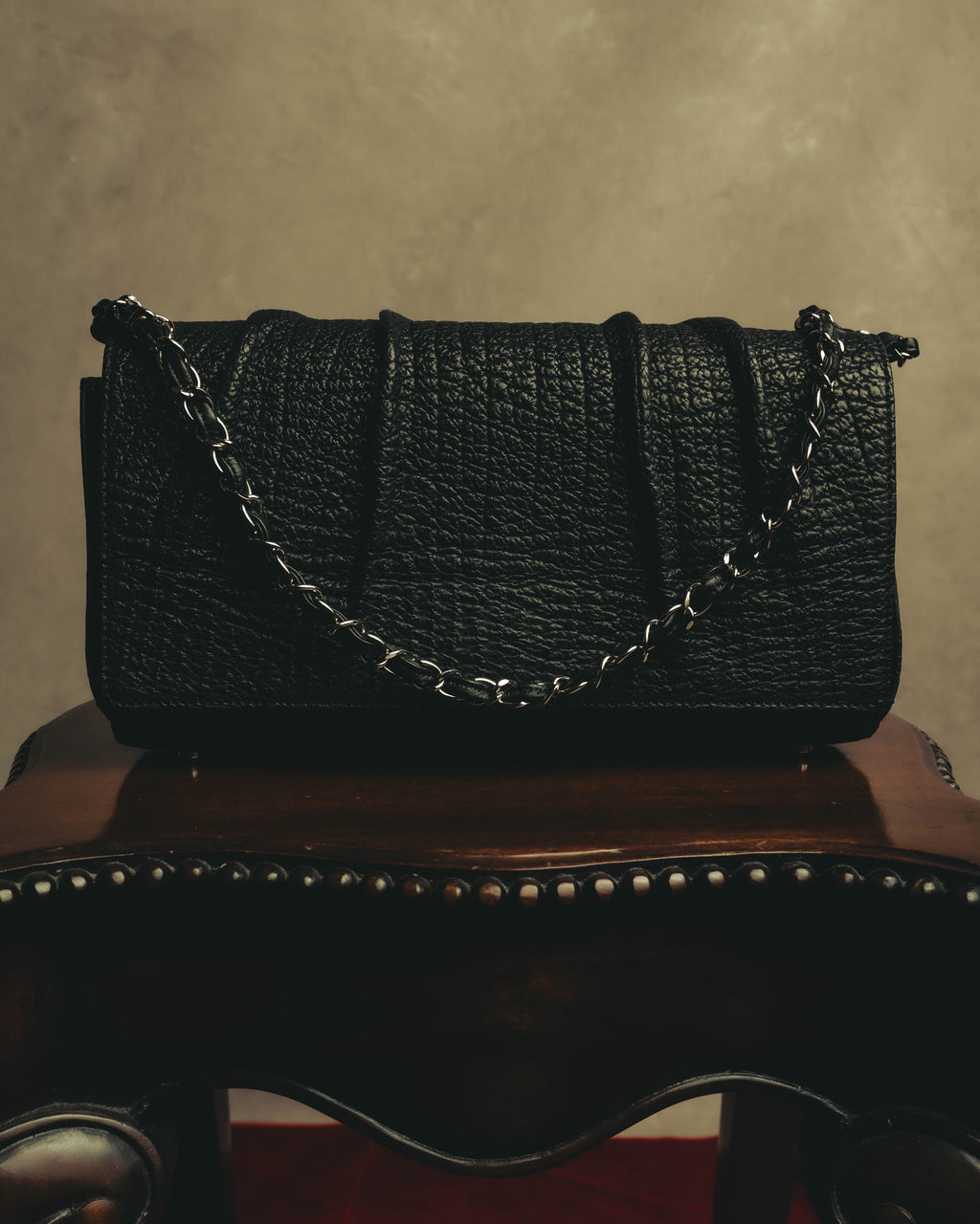 ブラックレザーのフラップ全体に施された四本の立体的な縦ラインと、前面に垂らしたシルバーカラーのチェーンショルダーストラップを捉えた正面カット。細かな凹凸が連なるシボの表情も確認できます。